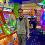Colorful arcade games surrounding a man standing next to a ticket game.